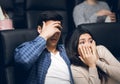 Young man with his girlfriend closing faces in terror while watching horror movie in cinema Royalty Free Stock Photo