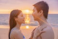 Young man and his girlfriend are looking into each other on a beach with a sea back and romantic sunset at Nai Thon Beach, Phuket