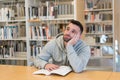 Young man with his head resting on his hand tired and bored of reading a book in the library