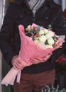 Young man holding beautiful bouquet of flowers closeup. Man wearing warm jacket and scarf. Unrecognizable people