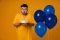 Young man holding birthday cake and blowing out candles while standing with blue air balloons isolated Royalty Free Stock Photo