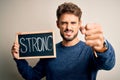 Young man holding blackboard with strong message standing over isolated white background annoyed and frustrated shouting with Royalty Free Stock Photo