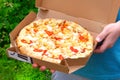 Young man is holding box with tasty pizza, close up view. Italian Cuisine. Snack on a sunny summer day Royalty Free Stock Photo
