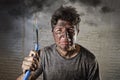 Young man holding cable smoking after electrical accident with dirty burnt face in funny sad expression Royalty Free Stock Photo