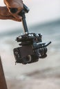 Young man holding camera attached to a steadicam on background of sea, a videographer shooting video walking on the beach, a