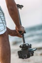 Young man holding camera attached to a steadicam on background of sea, a videographer shooting video walking on the beach, a