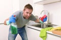 Young man holding cleaning detergent spray and sponge washing home kitchen clean angry in stress