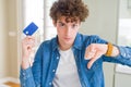 Young man holding credit card with angry face, negative sign showing dislike with thumbs down, rejection concept Royalty Free Stock Photo