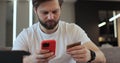 Young man holding credit card and smartphone sitting on couch at home. Man making a card payment on a smartphone. Online Royalty Free Stock Photo