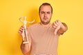 Young man holding figure of art dummy standing over isolated yellow background with angry face, negative sign showing dislike with Royalty Free Stock Photo