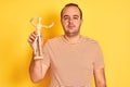 Young man holding figure of art dummy standing over isolated yellow background with a confident expression on smart face thinking