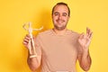 Young man holding figure of art dummy standing over isolated yellow background doing ok sign with fingers, excellent symbol Royalty Free Stock Photo