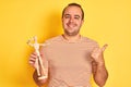 Young man holding figure of art dummy standing over isolated yellow background happy with big smile doing ok sign, thumb up with Royalty Free Stock Photo