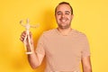 Young man holding figure of art dummy standing over isolated yellow background with a happy face standing and smiling with a Royalty Free Stock Photo
