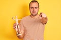 Young man holding figure of art dummy standing over isolated yellow background pointing with finger to the camera and to you, hand Royalty Free Stock Photo