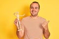 Young man holding figure of art dummy standing over isolated yellow background pointing and showing with thumb up to the side with Royalty Free Stock Photo