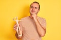 Young man holding figure of art dummy standing over isolated yellow background serious face thinking about question, very confused