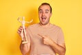 Young man holding figure of art dummy standing over isolated yellow background very happy pointing with hand and finger Royalty Free Stock Photo