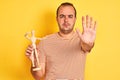 Young man holding figure of art dummy standing over  yellow background with open hand doing stop sign with serious and Royalty Free Stock Photo