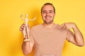 Young man holding figure of art dummy standing over  yellow background with surprise face pointing finger to himself Royalty Free Stock Photo