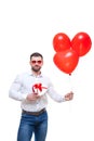 Young man holding gift box and balloons over white background. with glasses in the shape of heart. Looking at camera Royalty Free Stock Photo