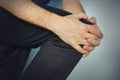 young man is holding his hands over his sick knee on a blue background. patella fracture, athlete in a tracksuit with a pain in th Royalty Free Stock Photo