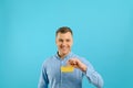 A young man holding a mini shopping cart and standing in front of a blue background in the studio. Sales concept. Place for text