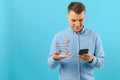 A young man holding a mini shopping cart and standing in front of a blue background in the studio. Sales concept. Place for text