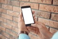 Man holding mobile phone with blank screen in hands near brick wall Royalty Free Stock Photo