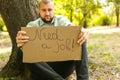 Young man holding piece of cardboard with text NEED JOB outdoors Royalty Free Stock Photo