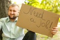 Young man holding piece of cardboard with text NEED JOB outdoors Royalty Free Stock Photo