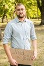 Young man holding piece of cardboard with text NEED JOB outdoors Royalty Free Stock Photo