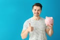 Young man holding piggy bank on color background. Savings money concept Royalty Free Stock Photo