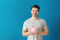 Young man holding piggy bank on color background. Savings money concept Royalty Free Stock Photo