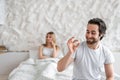 Young man holding pill, solving sexual dysfunction problems, happy woman sitting in bed and waiting for her husband Royalty Free Stock Photo