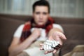 Young man holding pills in his hand sitting on the sofa with handkerchief looking sick illness at home Royalty Free Stock Photo