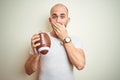 Young man holding rugby american football ball over isolated background cover mouth with hand shocked with shame for mistake, Royalty Free Stock Photo
