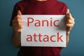 Young man holding sheet of paper with words PANIC ATTACK on color background