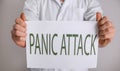 Young man holding sheet of paper with words PANIC ATTACK on light background