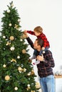 Young man holding on the shoulders little boy, dad and son decorating Christmas tree on the eve of holidays. Royalty Free Stock Photo