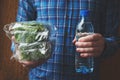 Man holding single use blue plastic bottle of mineral water and fresh green salad
