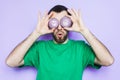 Young man holding slices of red onion in front of his eyes