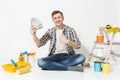 Young man holds bundle of dollars, cash money, sits on floor with instruments for renovation apartment isolated on white Royalty Free Stock Photo