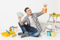 Young man holds bundle of dollars, cash money, sits on floor with paint can, instruments for renovation apartment Royalty Free Stock Photo