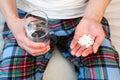 Young man holds handful white pills and glass of water in hands. Taking supplements, antibiotic, antidepressant medication.