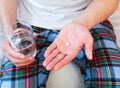 Young man holds one pill and glass of water in hands. Taking antibiotic, antidepressant, painkiller medication. Close-up Royalty Free Stock Photo