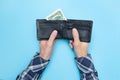 Young man holds a wallet in which there are only two dollars. Blue background. Bankrupt. Money is tight. Importance of