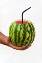 A young man holds a whole watermelon with a straw for drinking,