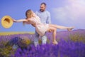 Young man holds woman in lavender field, cute young couple in love walking in a field of lavender flowers. Girl raises her hat up Royalty Free Stock Photo