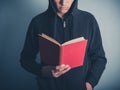 Young man in hooded top reading red book